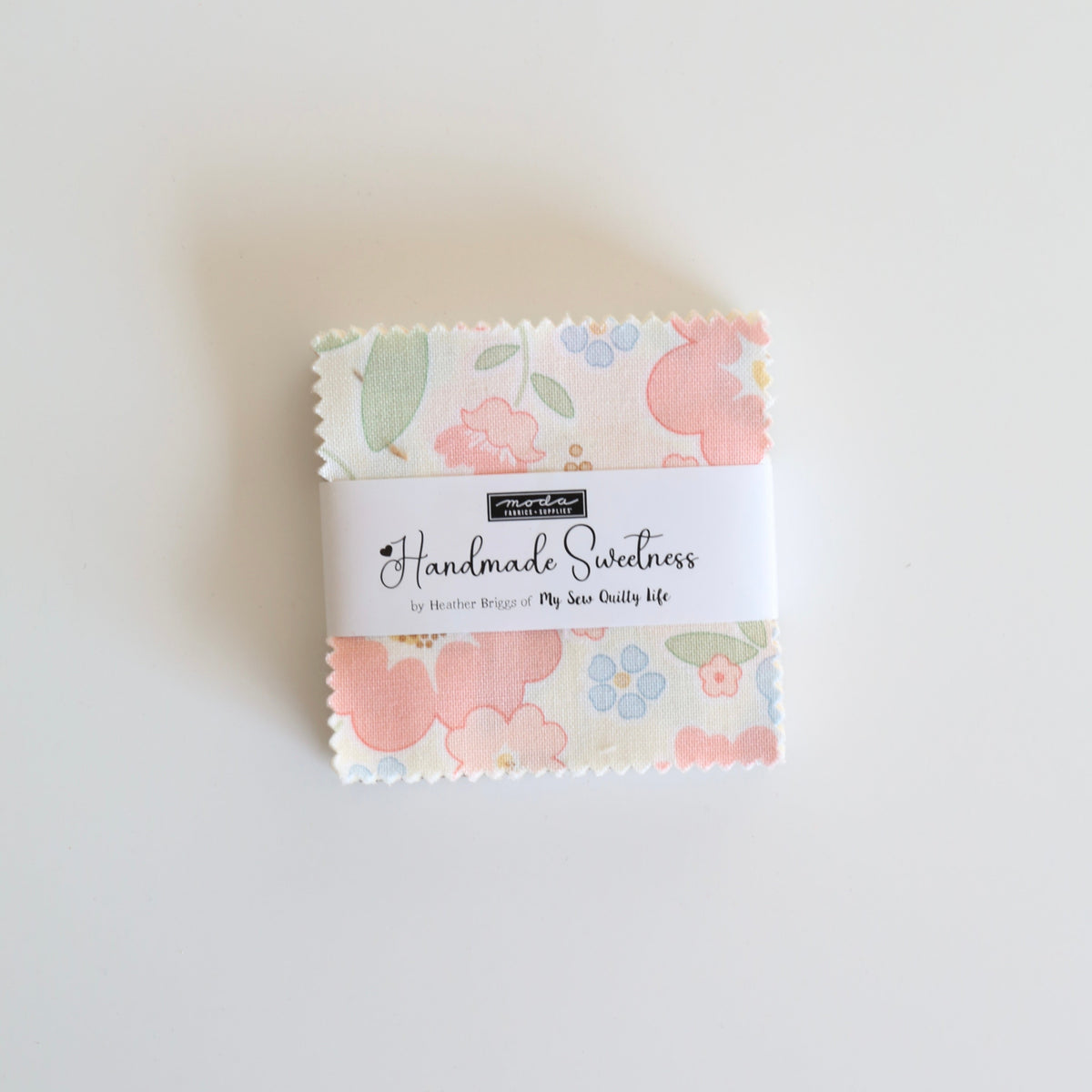 A small bundle of floral-patterned fabric strips wrapped with a white paper band labeled 'Handmade Sweetness' and 'The Hot Scallops', photographed on a plain white background.
