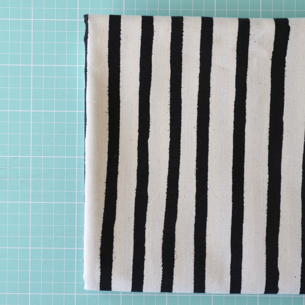 A folded piece of fabric with vertical black stripes on a white base, placed on a light blue cutting mat with grid lines.