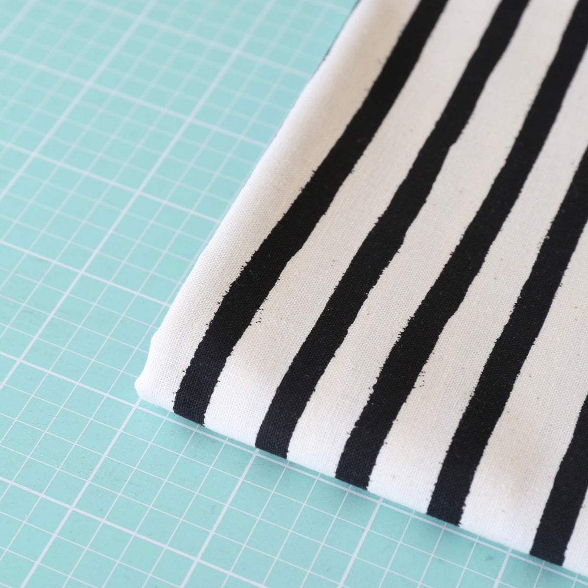 A folded piece of fabric with bold black vertical stripes on a white base, placed on a mint green cutting mat with a grid pattern.