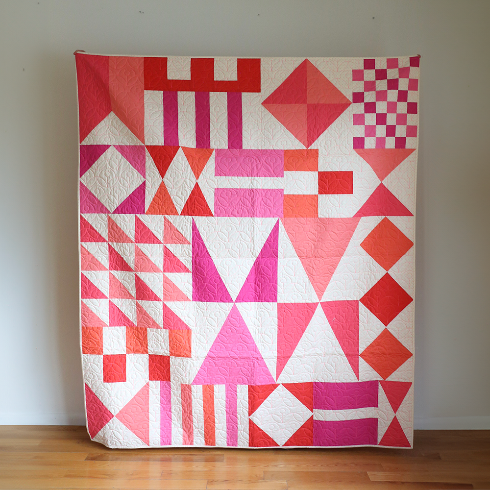 Geometric quilt with red, pink, and white pattern on a plain background
