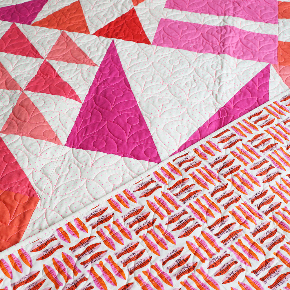 Quilt with geometric patterns in pink, red, and white.