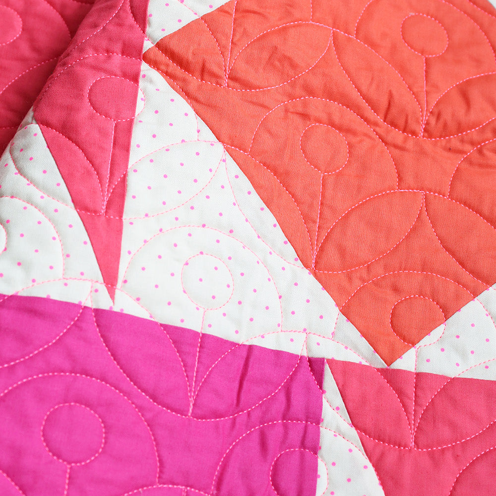 Quilt with pink, orange, and white geometric pattern on a white background