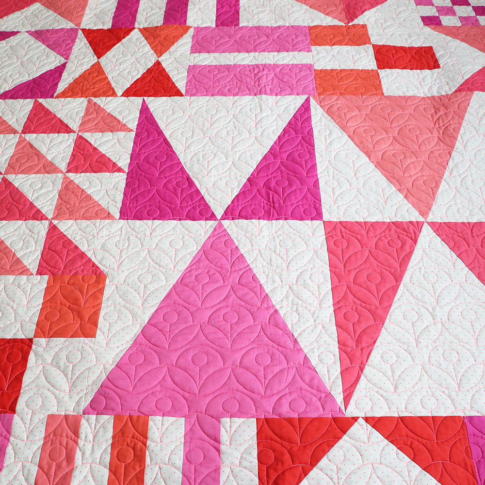 Quilt with geometric pattern in pink, red, and white on a wooden surface