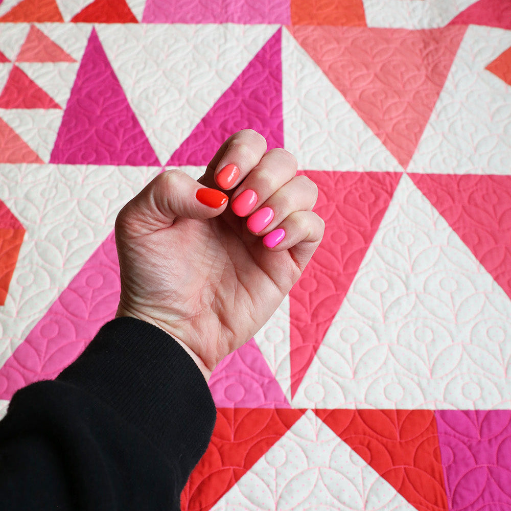 Hand with red nail polish on a colorful geometric quilt