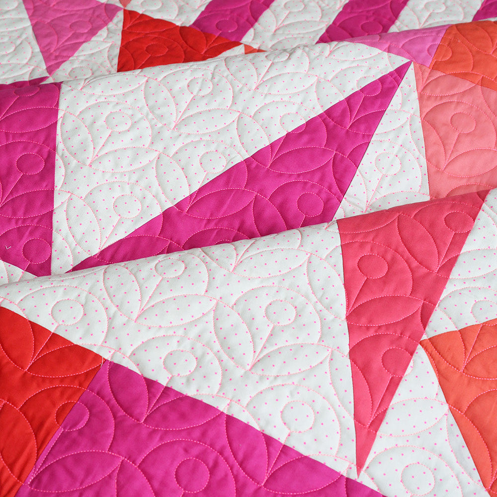 Quilt with pink, red, and white geometric pattern on a wooden surface