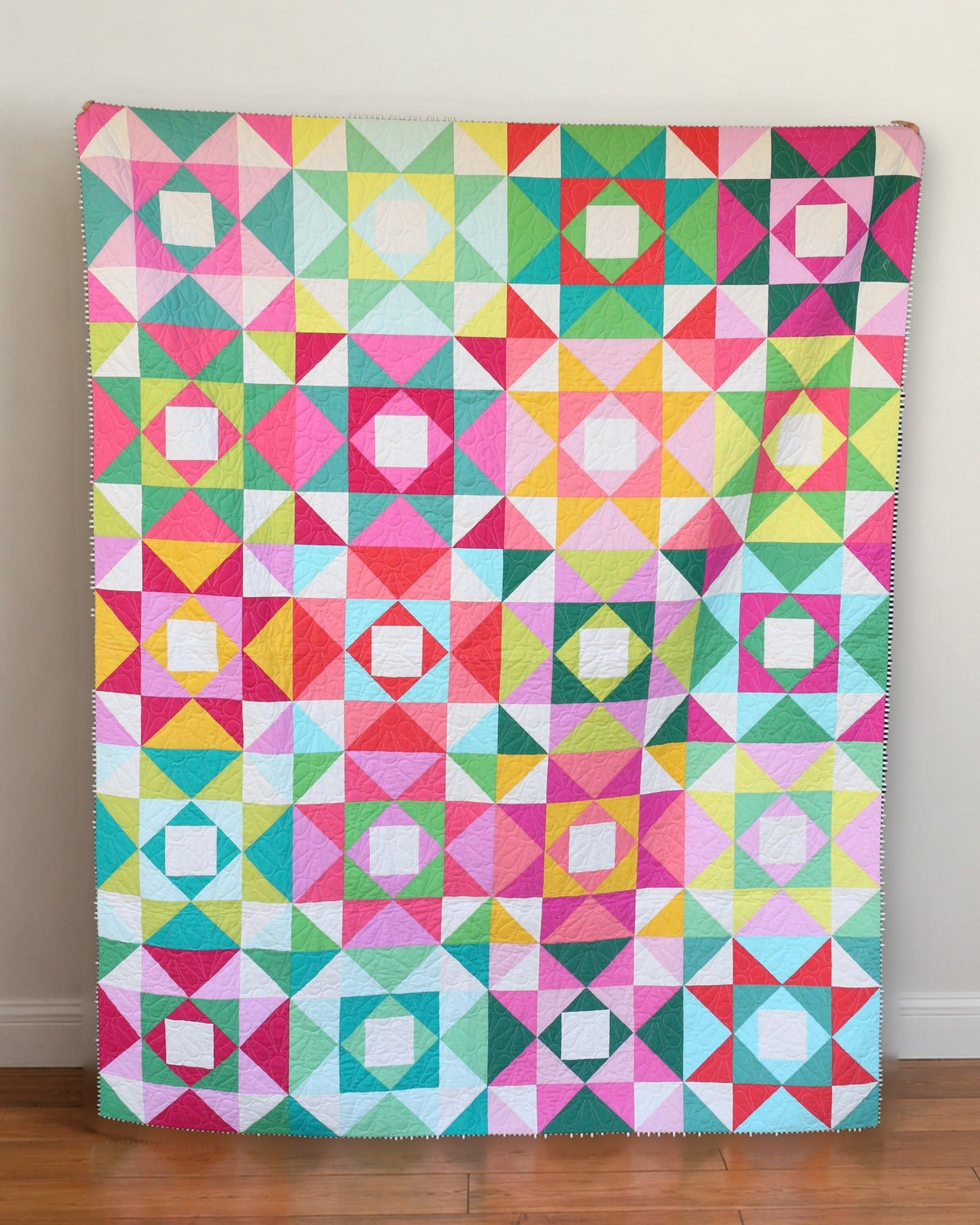 Economy Stars scrappy quilt leaning against a cream wall on a wood floor